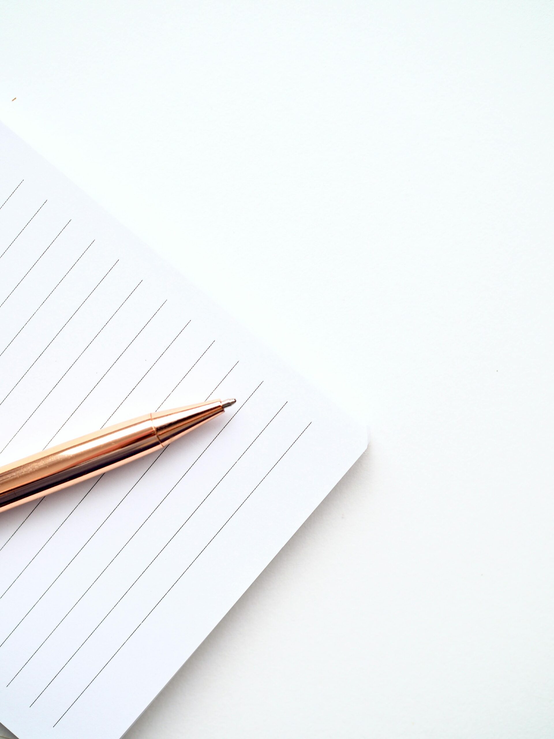 A close-up shot of a gold pen on a lined notepad with a white background, offering ample copyspace.